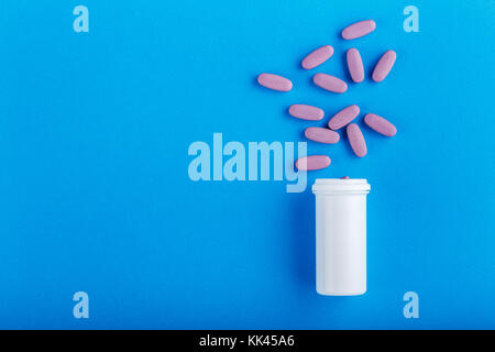 pills poured from a plastic jar on a blue background, top view, space for text Stock Photo