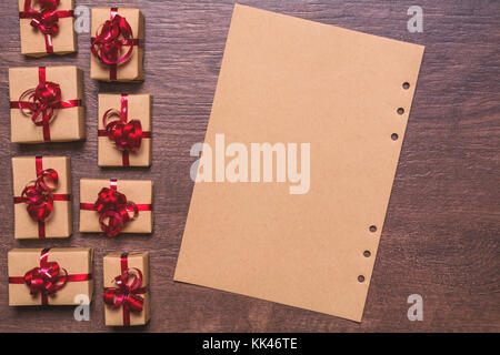 gifts wrapped in kraft paper and red ribbon and bow, paper for empty space for text on a wooden background. View from above, flat lay design. Stock Photo