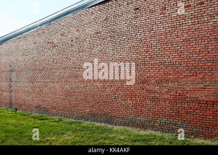 High red brick wall background texture of a building or perimeter boundary with a neat mowed grass lawn in the foreground in an angled view Stock Photo