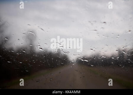 Beads of water from rain condensed on a window pane looking through the glass to the blurred scene outdoors with grey clouds Stock Photo