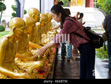 A woman pours water on a stature at Wat  Phra Sing Temple, a Buddhist temple inside the Old City walls of Chiang Mai, Thailand. Stock Photo