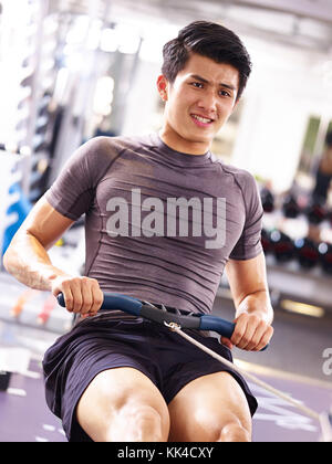 young asian adult man working out in gym using rowing machine. Stock Photo