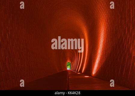 Empty long arched brick pedestrian tunnel, Prague. Orange brick walls, strip of lighting lamp. Bright arch. Underground mysterious footpath for walker Stock Photo