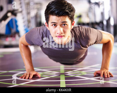 young asian adult man exercising in gym doing pushups, frontal view. Stock Photo
