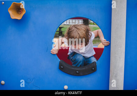 A little girl climbs on playground equipment on summer day Stock Photo
