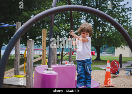 A little girl climbs on playground equipment on summer day Stock Photo
