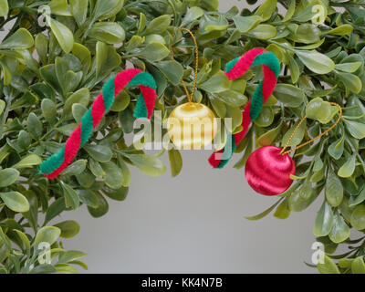 Christmas wreath or garland made by plastic leaf decorated by red and white cane and red and yellow apple in close up isolated on white background Stock Photo
