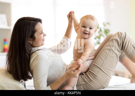 Mom and baby boy in diaper playing in sunny room. Mother and little kid relaxing at home. Family having fun together. Stock Photo