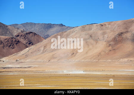 Dust from a car driving in the dry landscape at Tso Kar with scenic himalayan peaks in the back, Ladakh, Jammu and Kashmir, India. Stock Photo