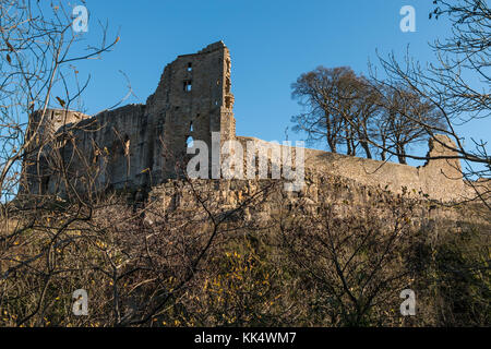 The remains of the 12th century Barnard Castle on a rocky outcrop above the river Tees, in strong winter sunshine against a clear blue sky background. Stock Photo