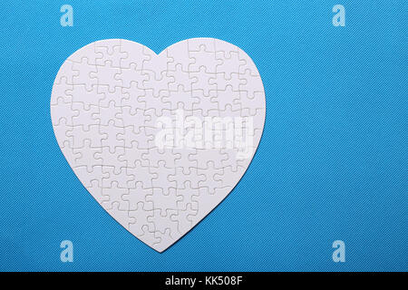 White details of a puzzle on blue background. A puzzle is a puzzle from small pieces. Heart shape of the details. Hands folding puzzle in white. Stock Photo