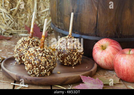 Caramel apples coated with nuts on a wooden plate with fresh apples Stock Photo
