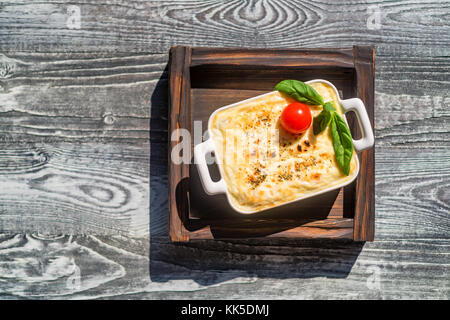 Tasty lasagna in baking dish on wooden board Stock Photo