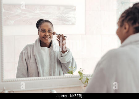 African woman applying foundation to her cheek in the bathroom Stock Photo