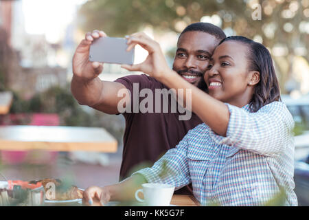 Young African couple taking selfies at a sidewalk cafe Stock Photo