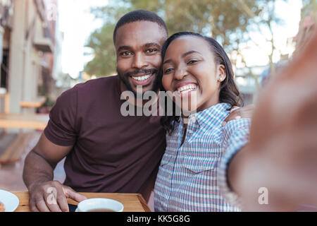 Smiling young African couple taking selfies together at a cafe Stock Photo