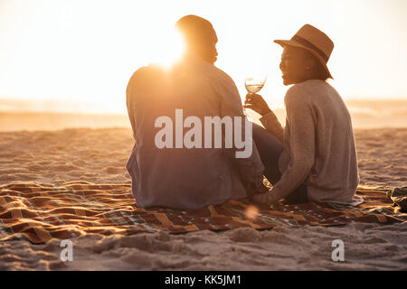Young African couple watching a beach sunset and drinking wine   Stock Photo