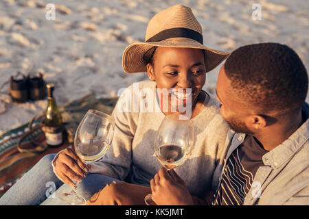 Happy young African couple drinking wine together at the beach Stock Photo