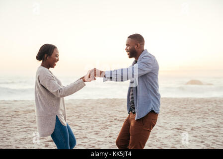 Smiling young African couple dancing on a beach at sunset Stock Photo