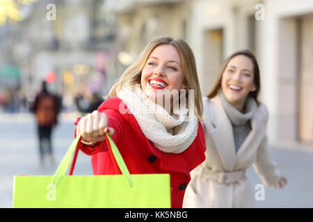 Two happy shoppers running searching shops outdoor on the street Stock Photo