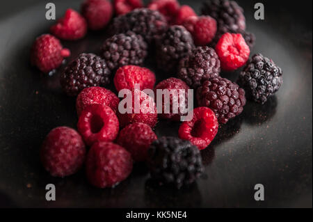 Frozen fruits on a black plate. Raspberries and blackberries Stock Photo