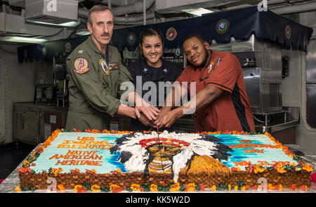 ATLANTIC OCEAN (Nov. 23, 2017) Capt. Joseph R. O'Brien, commanding officer of the amphibious assault ship USS Iwo Jima (LHD 7), cuts a cake with Aviation Ordnancemen 3rd Class Cassandra Blackhorn (center), and Culinary Specialist 3rd Class Daniel Brackett (right), during a National American Indian and Native Alaskan Heritage Month celebration. Iwo Jima, components of the Iwo Jima Amphibious Ready Group and the 26th Marine Expeditionary Unit are conducting a Combined Composite Training Unit Exercise that is the culmination of training for the Navy-Marine Corps team and will certify them for dep Stock Photo