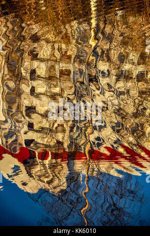 Reflection of houses in the water of the river. Abstract pattern created by the ripples. Stock Photo