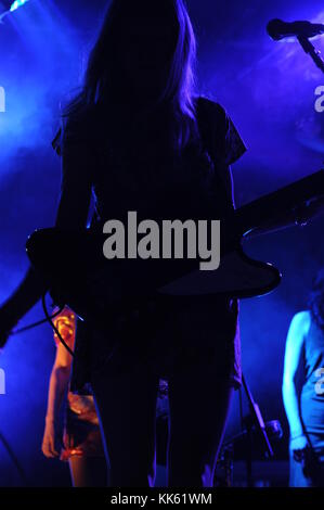 A female guitarist in a band silhouetted by blue stage lights Stock Photo