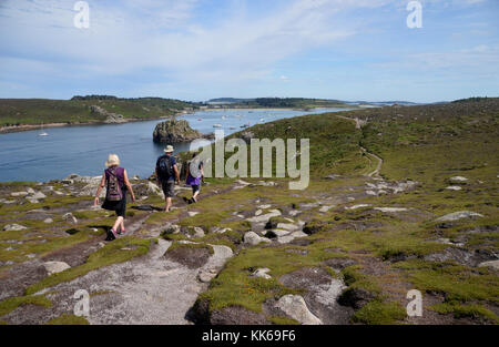 Three Hikers on the Coastal Path on Bryher Island Looking over to New Grimsby on Tresco in the Isles of Scilly, Cornwall, United Kingdom, UK. Stock Photo