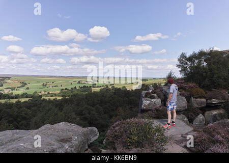 A young man looks out over thge countryside from a high vantage point in the summer in North Yorkshire in North East England on a summers day. Stock Photo