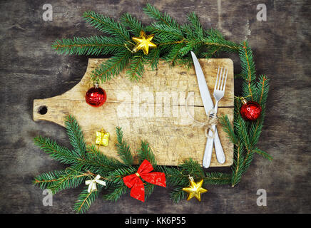Old cutting board with spruce branches on a wooden background with fork and knife kitchen cooking christmas Stock Photo