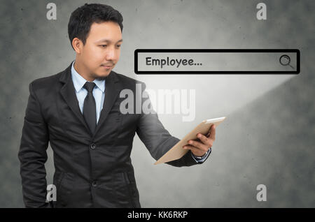 Asian businessman using the tablet with browsing of Internet searching “Employee” bar on the wall background, Internet concept Stock Photo