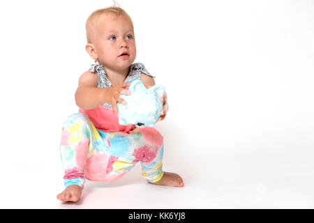 Cute toddler girl squatting on the floor is showing a saving piggy bank. All is on the white background. Horizontally. Stock Photo