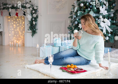 Blonde young woman with cup of hot chocolate in front of Christmas lights and Christmas tree Stock Photo