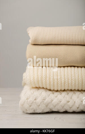 Pile of knitted clothes (sweaters, scarves, pullovers) white and beige colors. Selective focus. Stock Photo