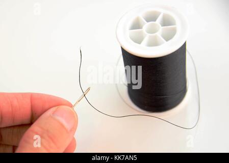 hand threading a needle with black thread Stock Photo