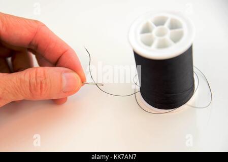 hand threading a needle with black thread Stock Photo