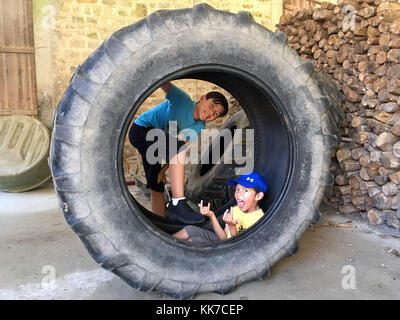 2 young boy brothers or friends playing in a farm in a giant tractor wheel tire Stock Photo