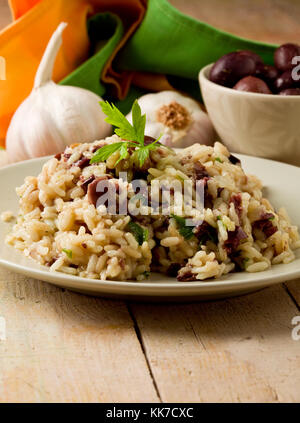 tasty risotto with black olives on wooden table with napkin and garlic ...
