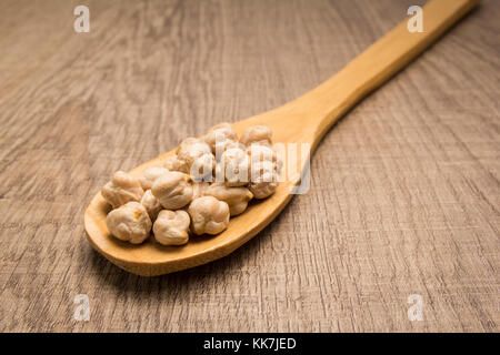 Cicer arietinum is scientific name of Chickpeas legume. Also known as Garbanzo bean, Chick Peas or Grao de Bico. Spoon and grains over wooden table. Stock Photo