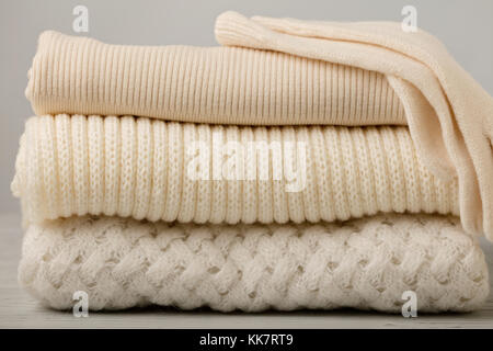 Pile of knitted clothes (sweaters, scarves, pullovers) white and beige colors. Selective focus. Stock Photo