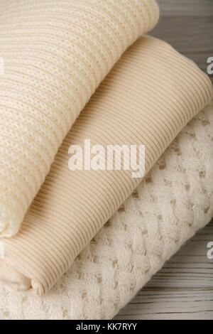 Pile of knitted clothes (sweaters, scarves, pullovers) white and beige colors. Selective focus. Stock Photo