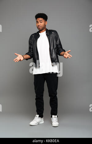 Full length photo of fashionable surprised african man standing with opened palms, looking at camera, isolated on gray background Stock Photo