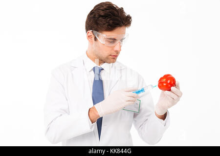 Close up portrait of a handsome young male scientist dressed in uniform making a syringe shot in a tomato isolated over white background Stock Photo