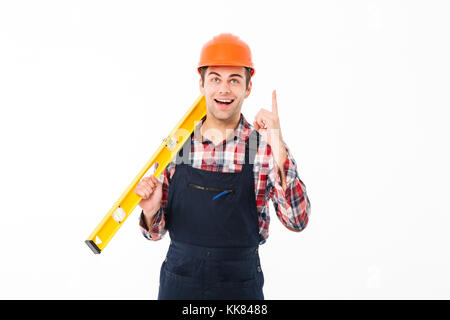 Portrait of an excited young male builder holding spirit level tool while standing and pointing finger up isolated over white background Stock Photo