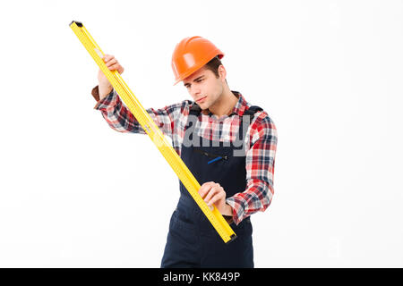 Full length portrait of a concentrated young male builder using spirit level tool while standing isolated over white background Stock Photo