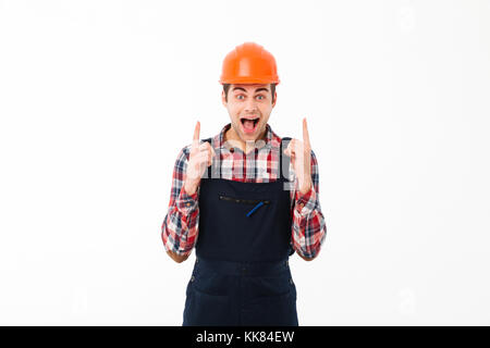 Portrait of an excited young male builder pointing two fingers up while standing and looking at camera isolated over white background Stock Photo