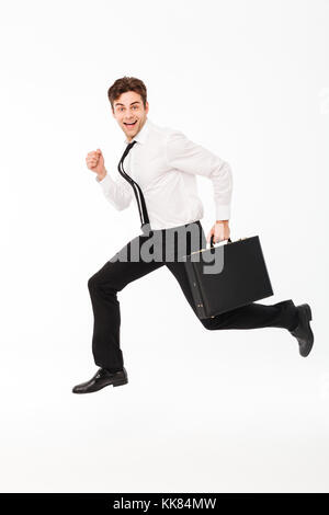 Full length portrait of a happy handsome businessman carrying briefcase while running and looking at camera isolated over white background Stock Photo