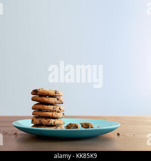 Warm chocolate chip cookies and stacked on a plate with crumbs on old wood table Stock Photo