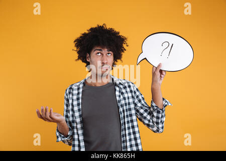 Portrait of a confused african man holding speech bubble and looking away isolated over orange background Stock Photo